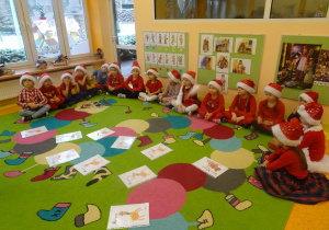 Grupa dzieci siedzi wokół ilustracji rozłożonych na dywanie.